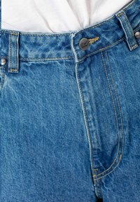 Vaqueros de mezclilla azul de talle alto, con costuras en contraste, cierre de botón y una textura ligeramente desgastada.