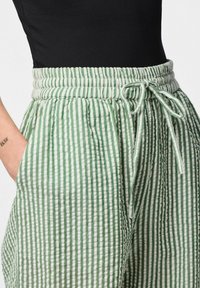 Groene en witte gestreepte wijde broek met een elastische tailleband, strikdetail en zijzakken. De stof lijkt lichtgewicht en textuur te hebben.