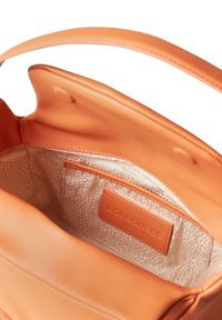 Orange leather handbag interior with a smooth finish, featuring a patterned lining and an inner pocket with a brand label.