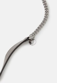 Collana in metallo con un accento in pelle grigia testurizzata, caratterizzata da un ciondolo circolare con un dettaglio a ritaglio triangolare.