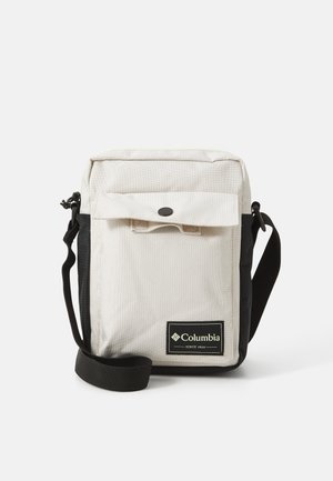Piccola borsa a spalla rettangolare beige e nera di Columbia con tasca frontale e tracolla nera regolabile su sfondo bianco.