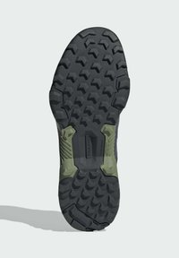 Tractionyttersula med ett robust svart gummimaterial, med ett geometriskt mönster och gröna accenter nära hälområdet för stabilitet.