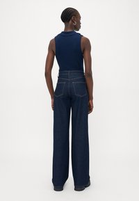 Mørkeblå ermeløs topp med krage, kombinert med høyhalsede, vide mørkeblå jeans med baklommer og subtile sømdetaljer.