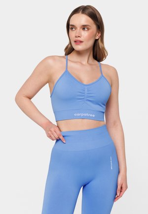 Light blue sports crop top with thin straps, ruching at the center, and matching high-waisted leggings featuring logo detail. Smooth fabric texture.