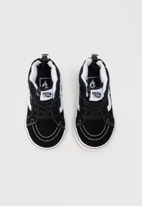 Crno-bijeli Vans tenisice za malu djecu s plišanom podlogom, crnim vezicama, bijelim šavovima i logotipom "Vans Off The Wall" na jeziku.