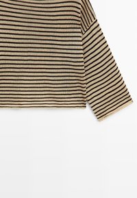 Chemise tricotée à manches longues rayée horizontale beige et noire avec ourlet droit, présentée sur un fond blanc.
