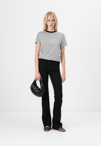 Striped black and white t-shirt paired with black flared jeans. The model holds a black handbag and wears leopard-print flats.