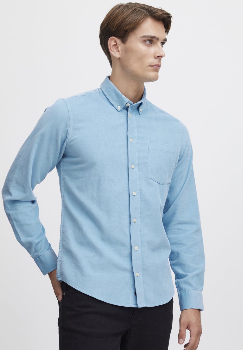 Vaaleansininen napillinen paita, joka on valmistettu teksturoidusta kankaasta. Siinä on kaulus, pitkät hihat ja rintatasku. Slim fit -malli, jossa on suora helma.
