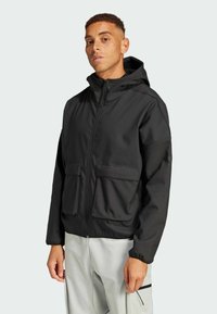 Black zip-up jacket with a hood, two front pockets, and a smooth texture. Designed with a relaxed fit and elastic cuffs.