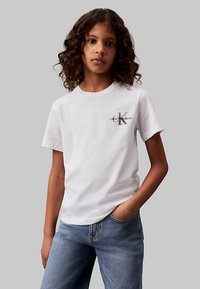 White cotton t-shirt with a round neckline and short sleeves, featuring a grey logo on the chest. Paired with blue denim jeans.