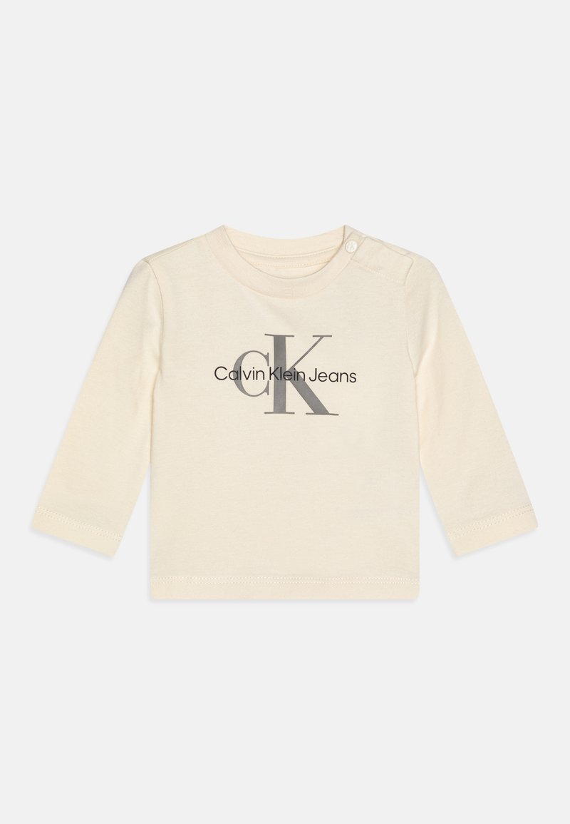 Bílý bavlněný tričko s dlouhým rukávem s šedým logem "CK" a textem "Calvin Klein Jeans." Obsahuje patentku na rameni.