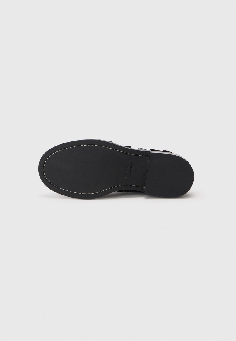 Suola di scarpa nera con finitura liscia e opaca. Cucitura bianca a contrasto lungo il bordino e una leggera curvatura alla punta per una forma ergonomica.