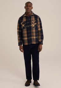 Geruite jas in marineblauw en beige flanel, met twee borstzakken, knoopsluiting en een kraag. Gepaarde met donkere broeken en brownboten.