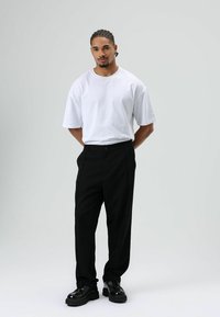 Wit katoenen T-shirt met korte mouwen, gecombineerd met zwarte broek met knoopsluiting en zwarte veterschoenen met een dikke zool.