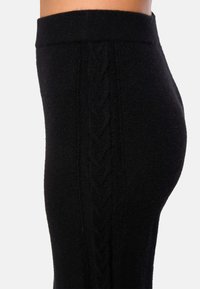 Des leggings tricotés noirs présentent une taille côtelée et un motif en maille torsadée courant verticalement sur le côté. Texture douce, design ajusté.