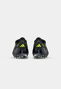 Black and neon green sports shoes with a textured upper, padded collar, and a hard plastic heel counter; features raised studs on the outsole.