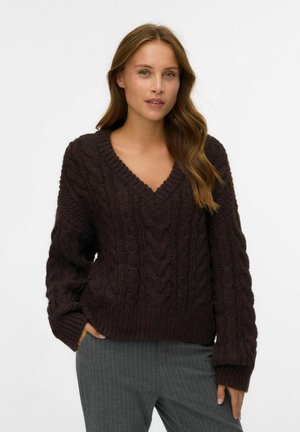 Dunkelbrauner, grob gestrickter Pullover mit V-Ausschnitt, der strukturierte Zopfmuster, gerippte Bündchen und Saum aufweist. Der Stoff wirkt weich und gemütlich.