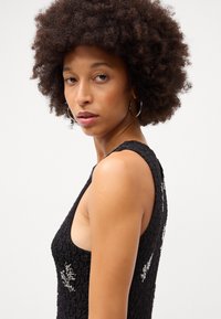 Top fără mâneci, de culoare neagră, cu textură, prezentând detalii brodate complicate. Design strâns, cu guler rotund și laterale deschise.