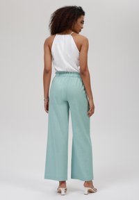 Top halter blanco ligero combinado con pantalones anchos de color verde menta con una cinturilla elástica. Textura suave, diseño minimalista.
