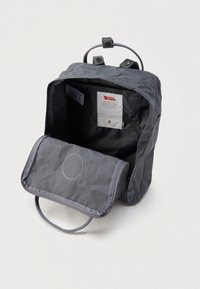 Γκρι σακίδιο με υφή και ανθεκτική επιφάνεια. Διαθέτει κλείσιμο με καπάκι, χειρολαβή στην κορυφή και εσωτερική ετικέτα με λεπτομέρειες για το υλικό και τη φροντίδα.