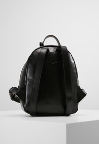 Sac à dos en cuir noir de forme arrondie, doté de bretelles réglables, d'une surface texturée et d'un détail triangulaire à l'arrière.