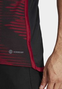 Punainen ja musta urheilupaita vaakasuorilla raidoilla, AEROREADY-logo ja erottuva punainen trimmi saumoissa, joka korostaa strukturoidun kankaan.