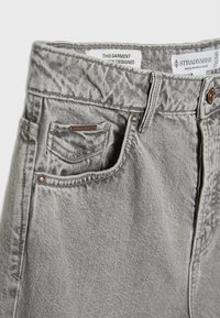 Jeans de mezclilla grises con cintura alta, diseño de cinco bolsillos y detalles de costura sutiles. Incluye etiqueta de la marca en el bolsillo delantero.