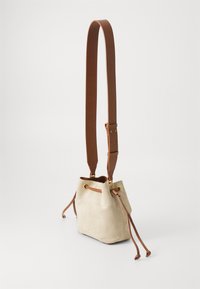 Borsa bucket in suede beige con manici in pelle marrone, presenta occhielli dorati e tracolla regolabile. Design semplice, chiusura con coulisse.