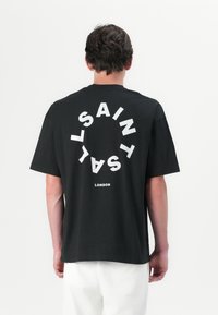 Svart bomull t-skjorte med stor hvit sirkulær tekst på baksiden som leser "SAINT LONDON," med korte ermer og løs passform.