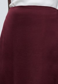 Gros plan d'une personne portant un haut blanc et une jupe unie bordeaux ou un tissu couvrant le bas du corps.