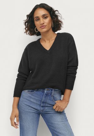 Schwarzer Strickpullover mit V-Ausschnitt und langen Ärmeln, kombiniert mit blauen Jeans. Der Stoff wirkt weich und strukturiert.