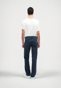 Sötétkék kordbársony nadrág, egyenes szabással, sima textúrával és hátsó zsebekkel. Fehér, rövid ujjú pólóval viselve.