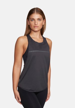 Kobieta z prostymi włosami, ubrana w bezrękawnik sportowy z siateczki w ciemnoszarym kolorze oraz czarne legginsy, stojąca na jasnym, jednolitym tle.