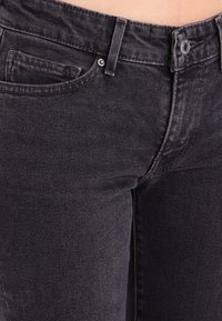Los jeans de mezclilla de un gris oscuro presentan un diseño ajustado con pierna recta, bolsillo frontal y cierre de botón metálico. La textura parece suave con un ligero desgaste.