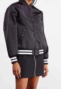 Schwarz bomberjacke aus glattem material mit geripptem kragen, gestreiften bündchen und saum. Verfügt über druckknöpfe und seitentaschen.