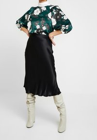 Green floral blouse with puffed sleeves, paired with a black satin skirt. Model wearing knee-high cream boots. Smooth textures, elegant design.