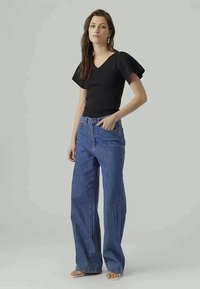 Black short-sleeve top with a v-neck, paired with light blue wide-leg jeans. The outfit is completed with beige slide sandals.