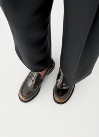 Smeđe kožne mokasinke s glatkim završetkom, blago sjajne, s kontrastnim svijetlosmeđim prstom i ukrasnim šavovima. Nošene s tamnim hlačama.