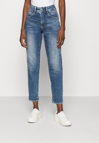 Jeans de mezclilla azul de cintura alta con un diseño de pierna recta, ligero desgastado y detalles de costura, combinados con zapatillas blancas.