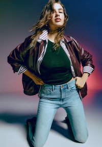 Bordo usnjeni bomber jakna preko črne prilegajoče majice, v kombinaciji s svetlo modrimi hlačami z visokim pasom, ki vsebujejo poškodovane detajle.