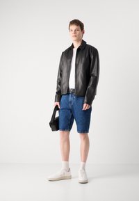 Svart skinnjakke, hvit t-skjorte, blå denimshorts, hvite sneakers og en svart veske. Enkelt design med avslappet passform og klassiske farger.
