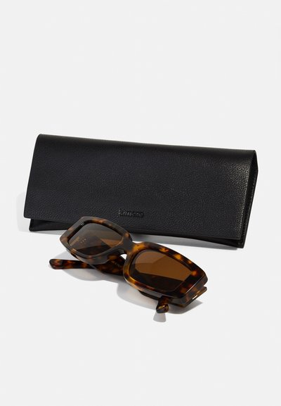 Brown tortoiseshell sunglasses with square frames and brown lenses, placed beside a black textured leather case.