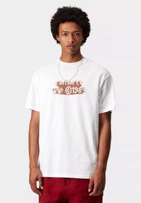 Biała bawełniana koszulka z krótkim rękawem, z wyraźnym nadrukiem w kolorze pomarańczowym i brązowym, okrągłym dekoltem i luźnym krojem. Noszona z srebrnym naszyjnikiem.