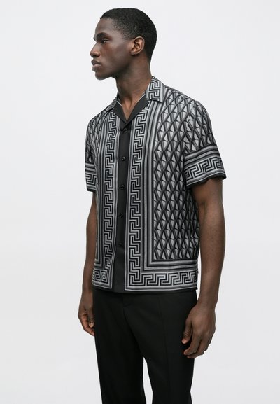 Πουκάμισο με κοντά μανίκια και γιακά σε μαύρο και γκρι με γεωμετρικό μοτίβο, διαθέτοντας κουμπιά μπροστά και αντίθετες υφασματικές λεπτομέρειες.