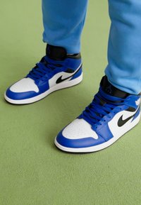 Visoke tenisice u plavoj, bijeloj i crnoj koži. Značajke uključuju perforiranu prednju čarapu, crni Swoosh logotip i sustav vezanja.