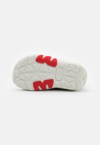 White sneaker outsole with textured grip, featuring red accents and a systematic pattern of grooves and shapes for traction.