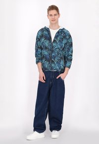 Hættejakke med sort baggrund og blåt bladmønster, parret med løstsiddende mørkeblå jeans og hvide sneakers.