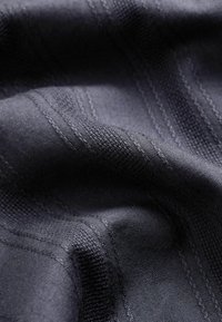 Ciemnogranatowa tkanina o gładkiej fakturze, z pionowymi paskami i subtelnymi wzorami tkanymi, podkreślająca wyrafinowany design.