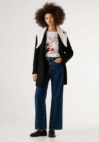 Črni plašč z belo umetno krzno ovratnikom, v kombinaciji z grafično majico, visokim pasom modrih kavbojk in črnimi loafer čevlji. Preprost, priložnostni videz.