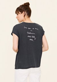 Dunkelgraues T-Shirt mit kurzen Ärmeln und lockerer Passform, mit weißem handgeschriebenem Text auf der Rückseite. Weicher Stoff, lässiges Design, sichtbare Nähte.